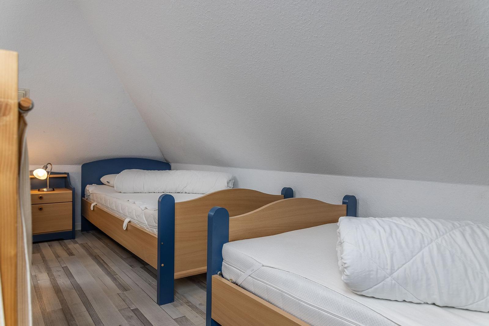 Zwei Betten mit weißen Matratzen und Kissen in einem Dachzimmer mit Holzboden und Nachttisch.