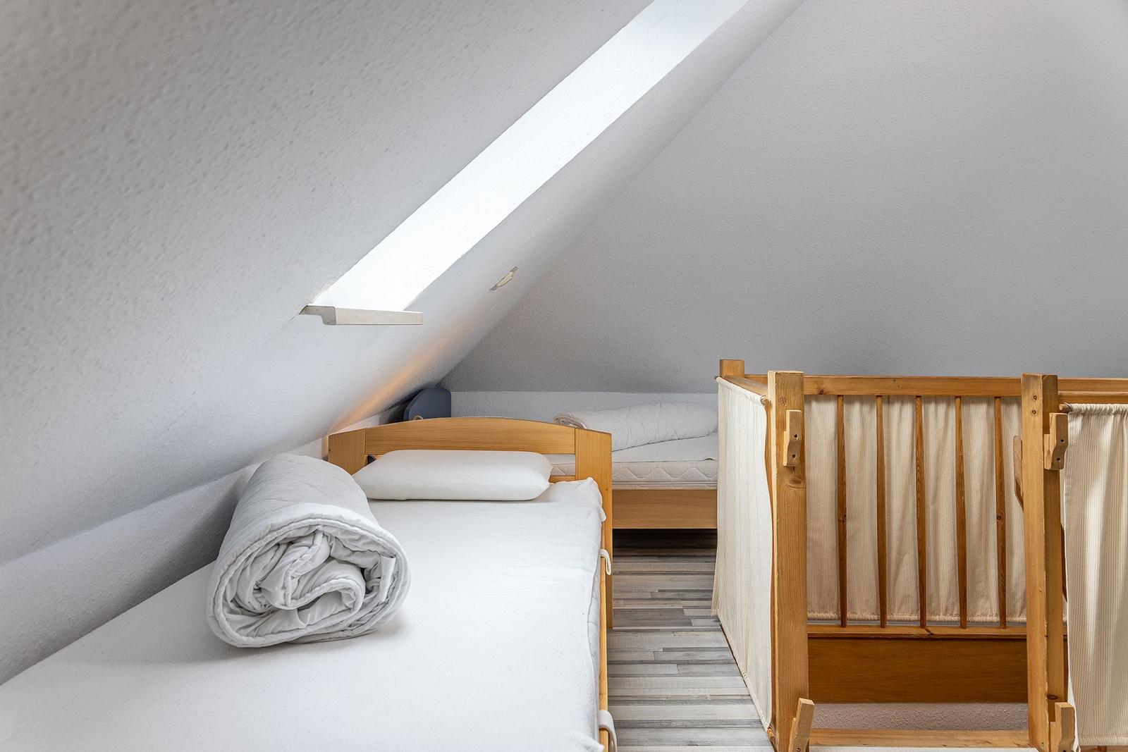 Zimmer mit Dachschräge, zwei Betten und einem Kinderbett.
