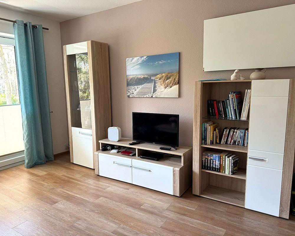Wohnzimmer mit Fernseher, Bücherregal und Fenster mit Vorhängen.