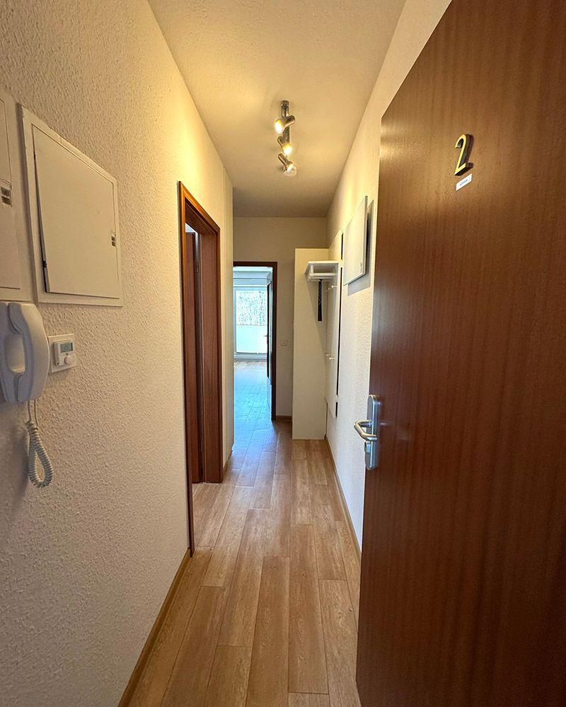 Flur mit Holzboden, Tür mit Nummer 2 und Wandtelefon.