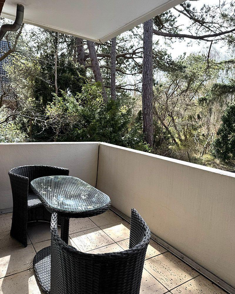 Balkon mit Tisch und zwei Stühlen, Blick in einen grünen Wald.