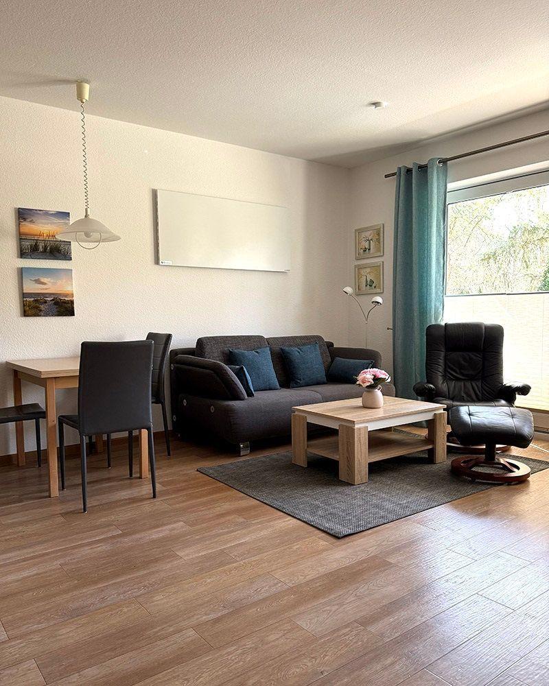 Wohnzimmer mit Sofa, Esstisch und Fenster mit Vorhängen.
