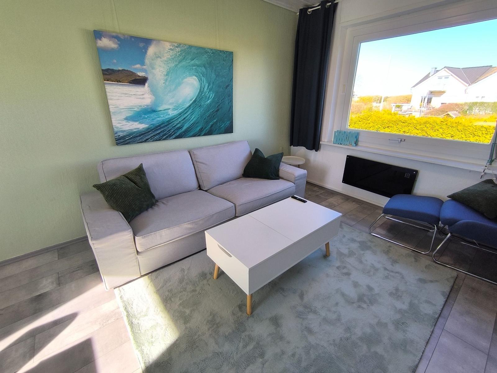 Wohnzimmer mit Sofa, Couchtisch und Wandbild. Fensterblick auf Garten.