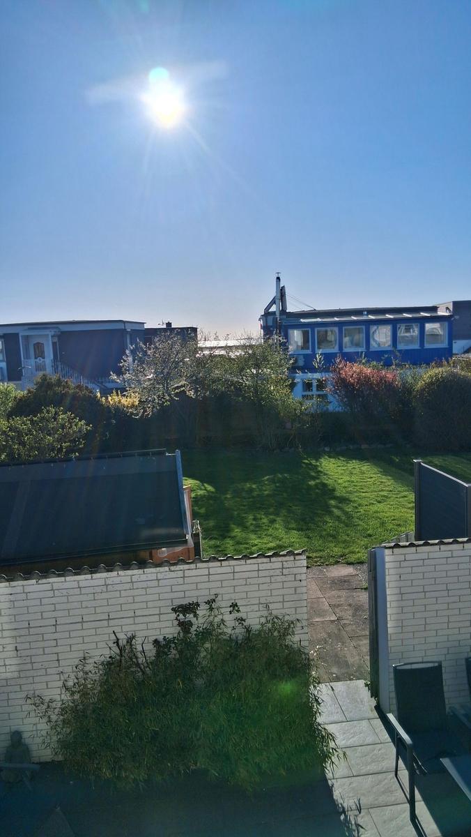 Hinterhof mit grünem Rasen, weißen Mauern und Blick auf blaue Gebäude unter blauem Himmel.