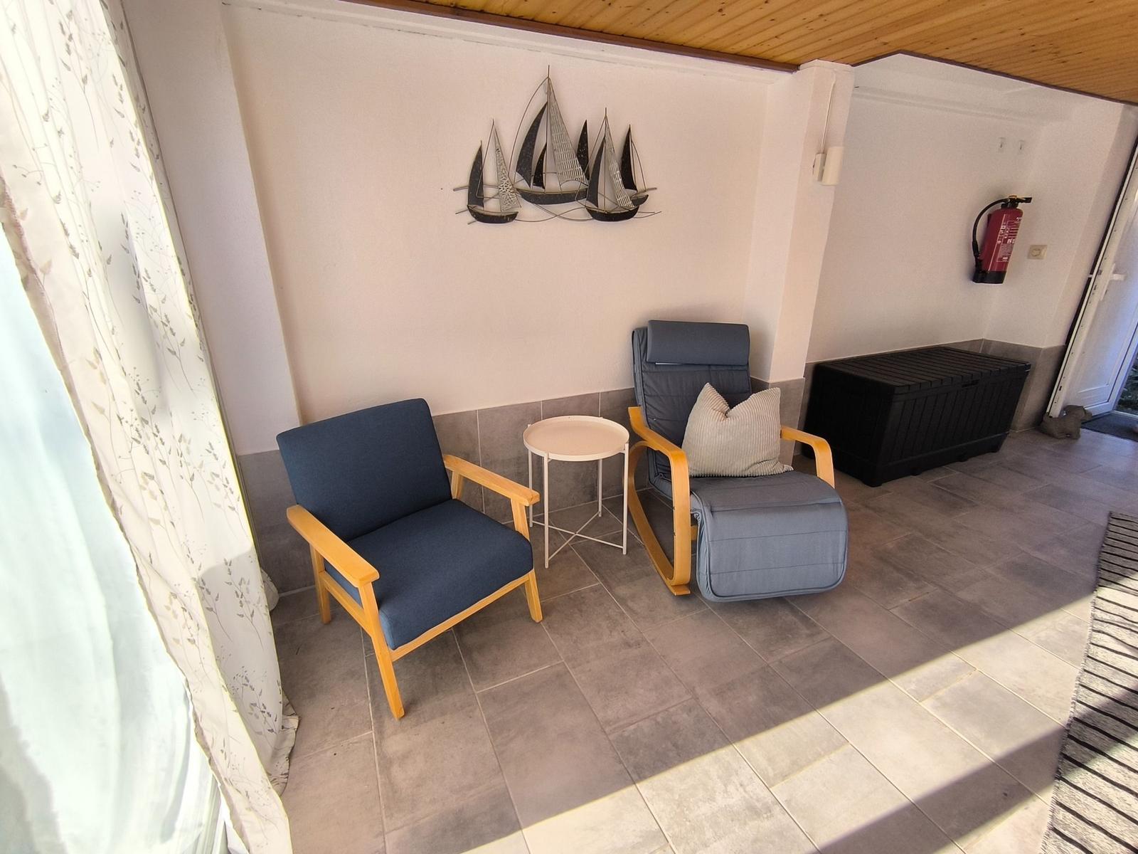 Zwei Sessel und ein kleiner Tisch stehen auf einer Terrasse mit Wanddekoration.