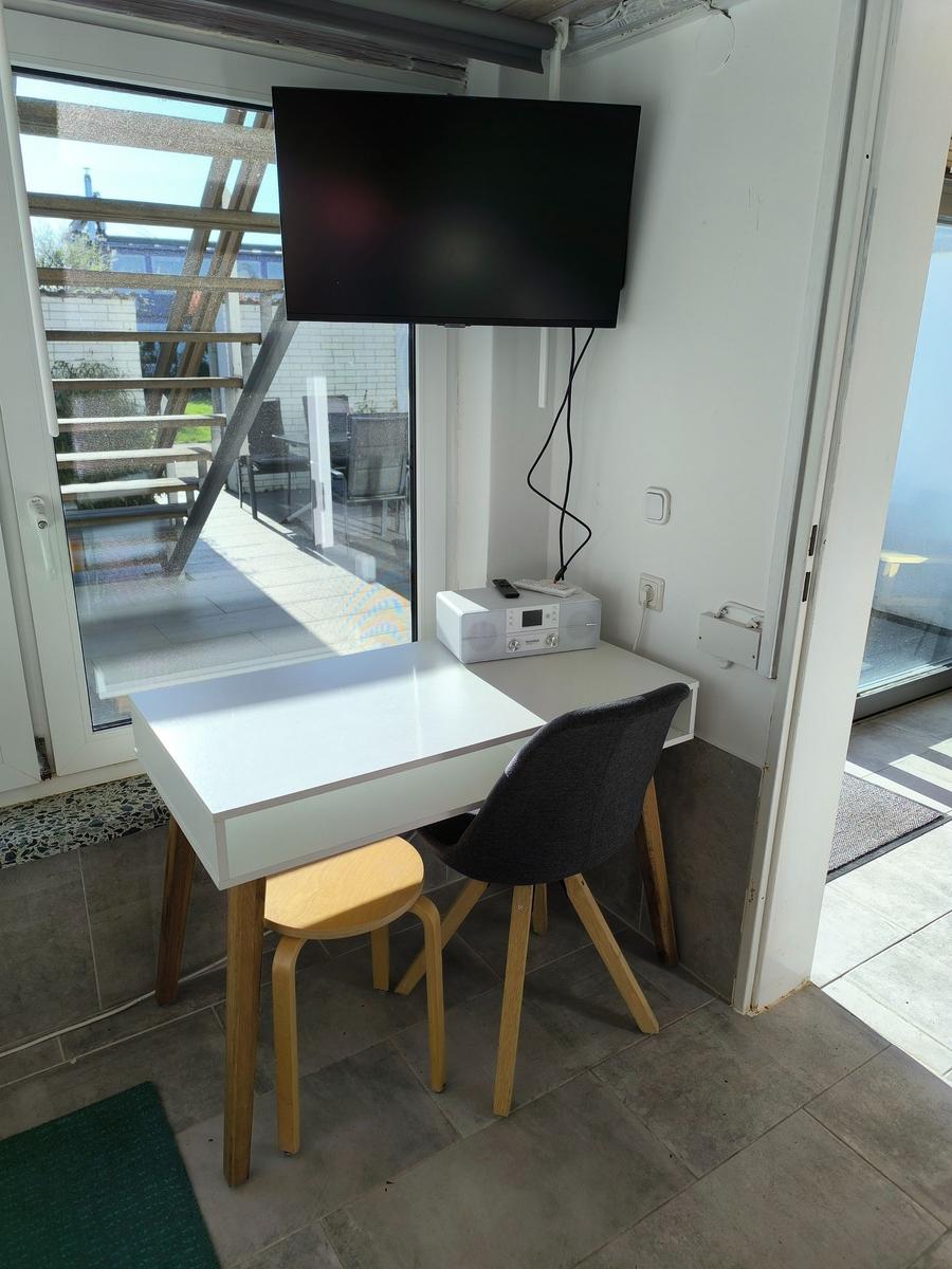 Arbeitsplatz mit Tisch, Stuhl und Fernseher. Blick auf Balkon.