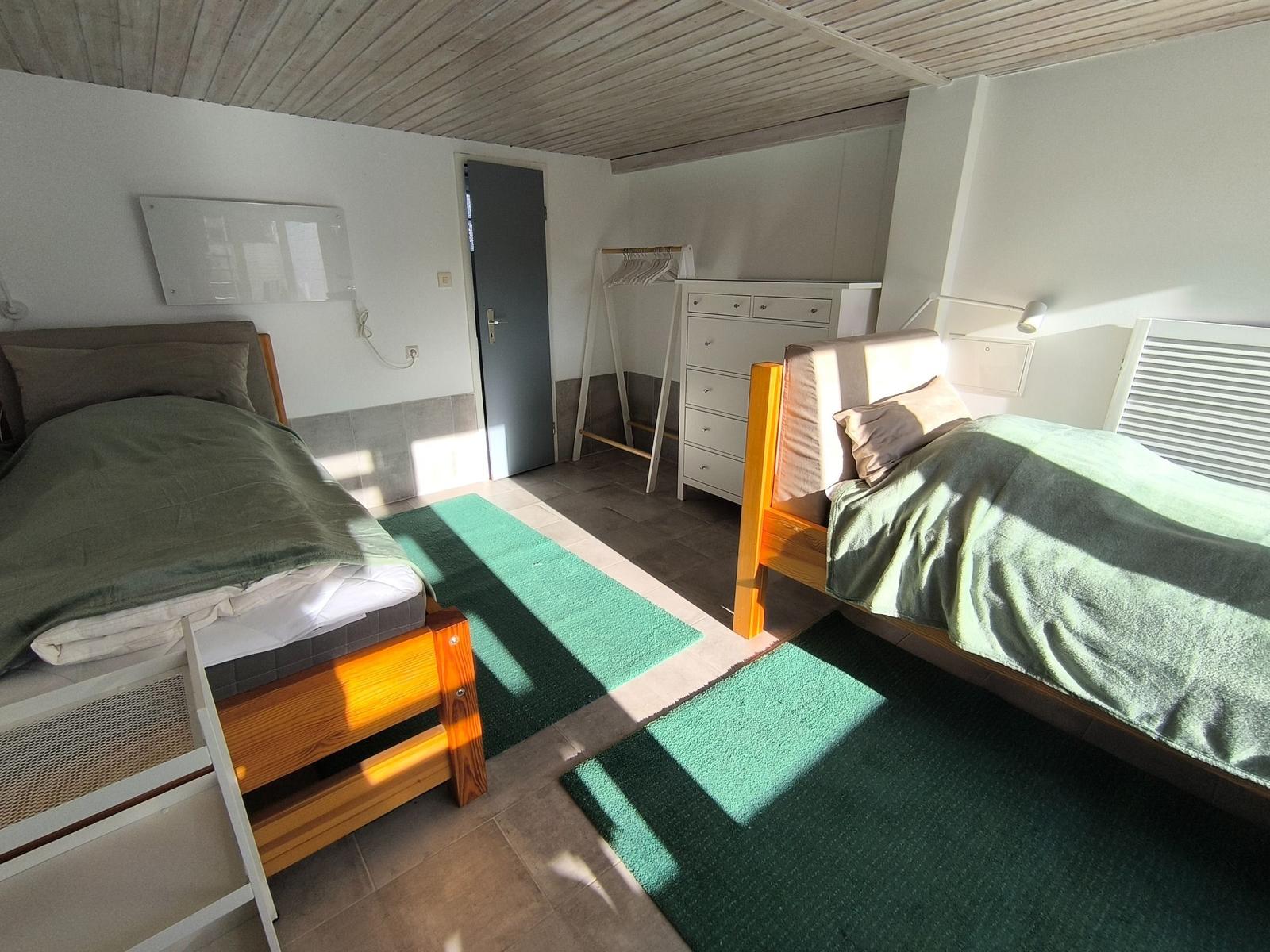 Zwei Betten mit grünen Bettdecken, Schrank und Kleiderständer im Raum.