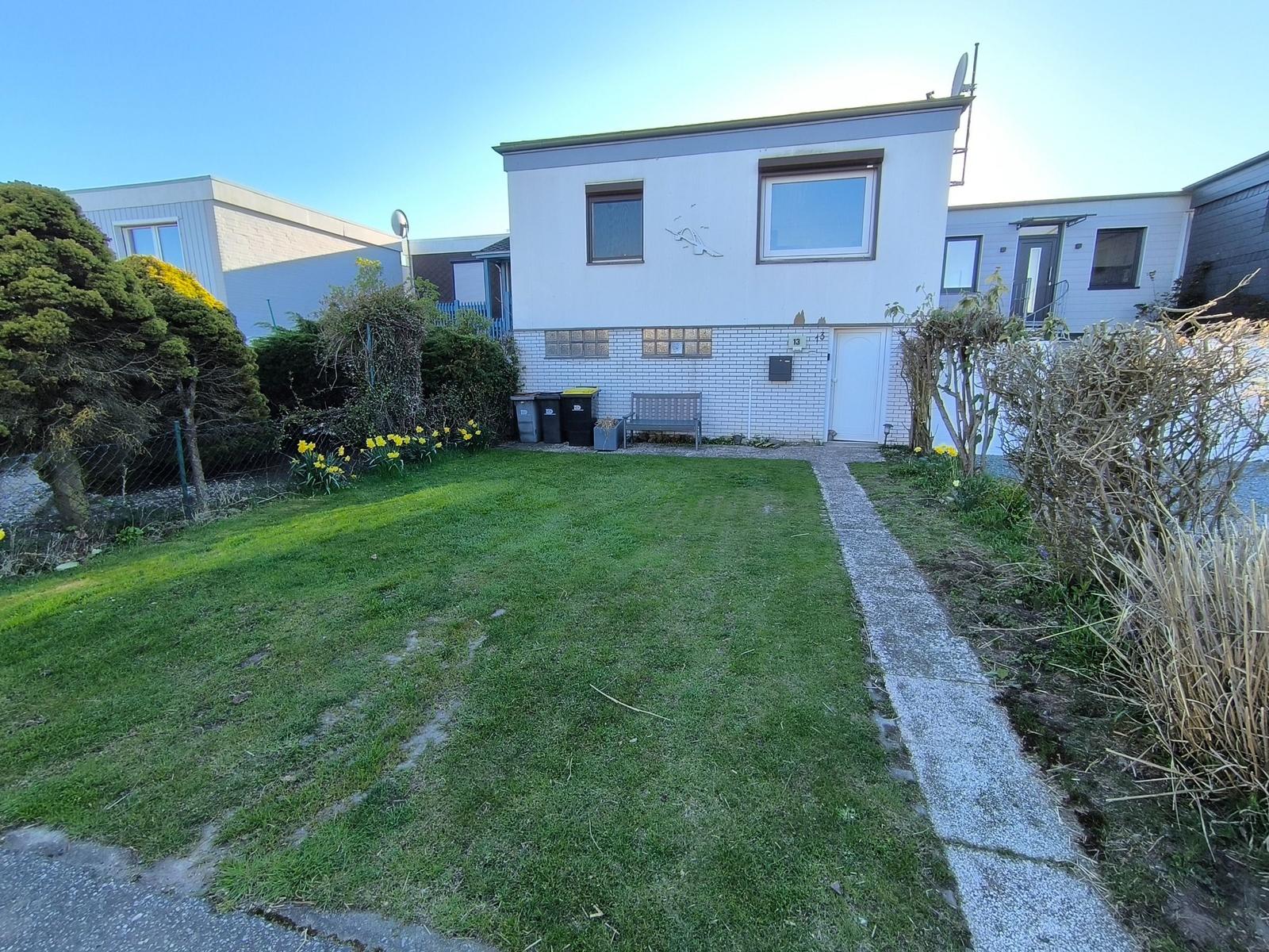 Ein zweistöckiges Haus mit Garten, Weg und Blumen. Die Fassade ist weiß mit Ziegeln.