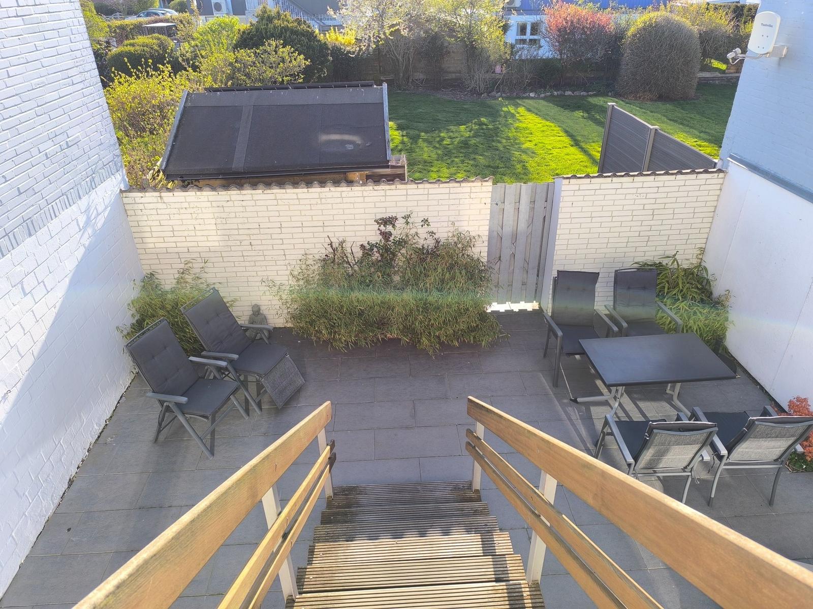 Terrasse mit Sitzgruppe, Tisch und Stufen zum Garten.