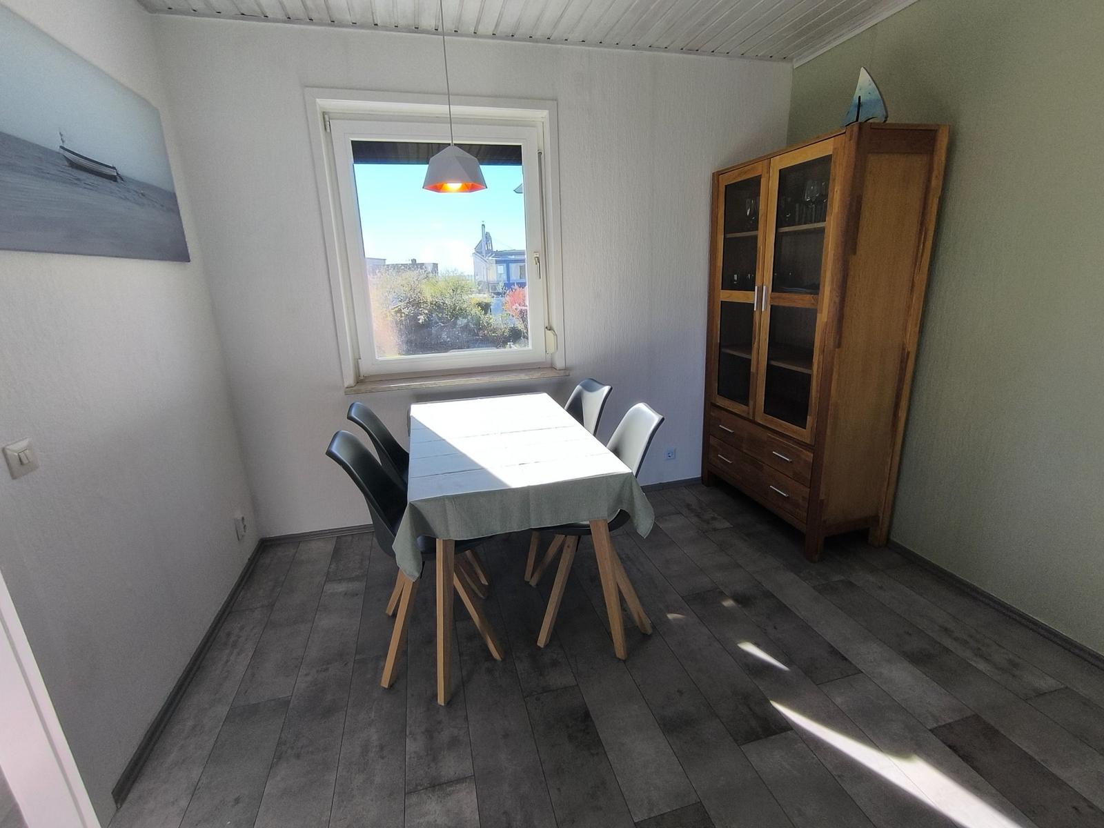 Esszimmer mit Tisch, Stühlen, Schrank und Fenster. Holzfußboden und Wandbild.