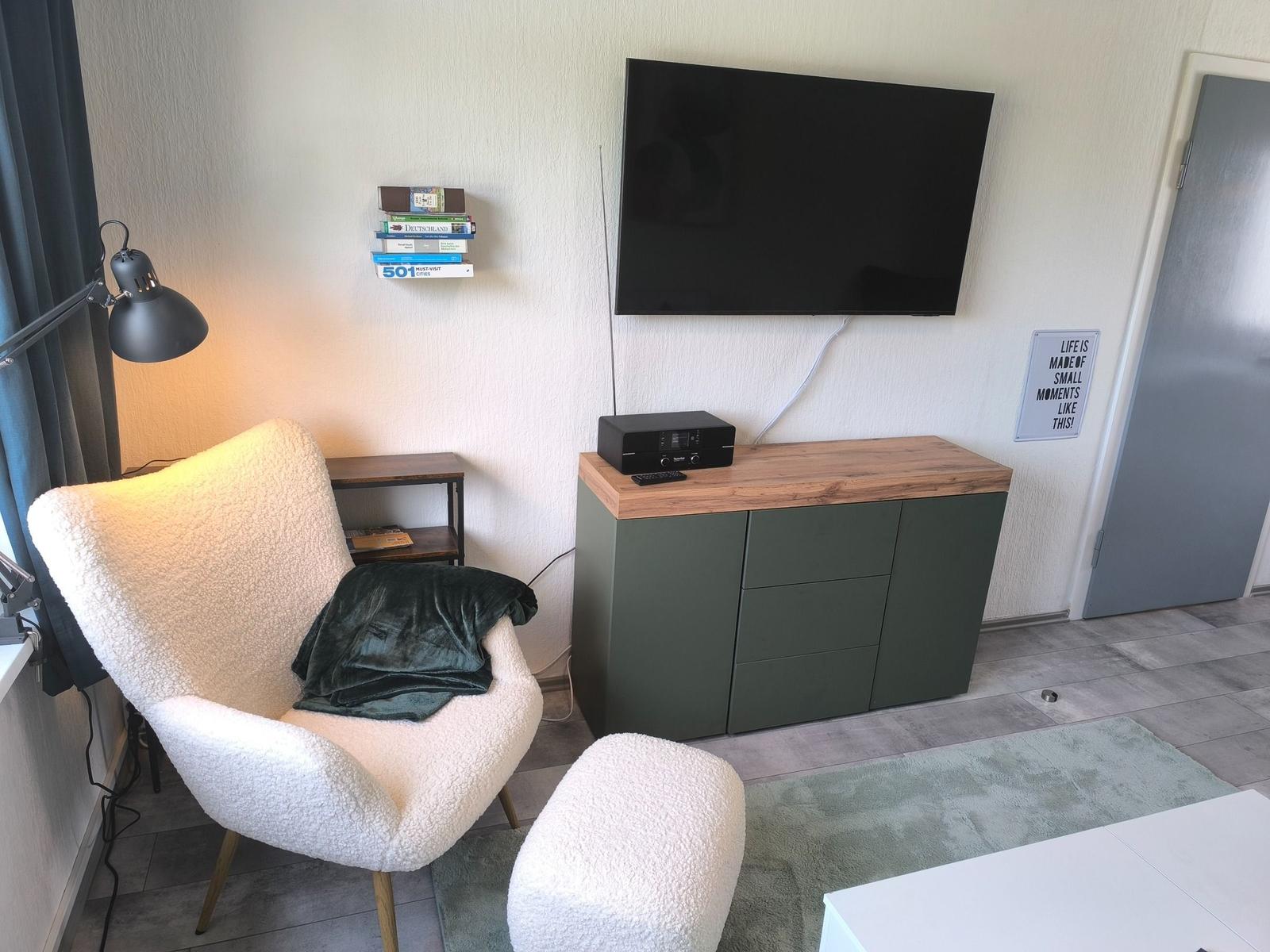 Ein Raum mit Sessel, Fernseher und Schrank. Auf dem Schrank steht ein Audio-Gerät.