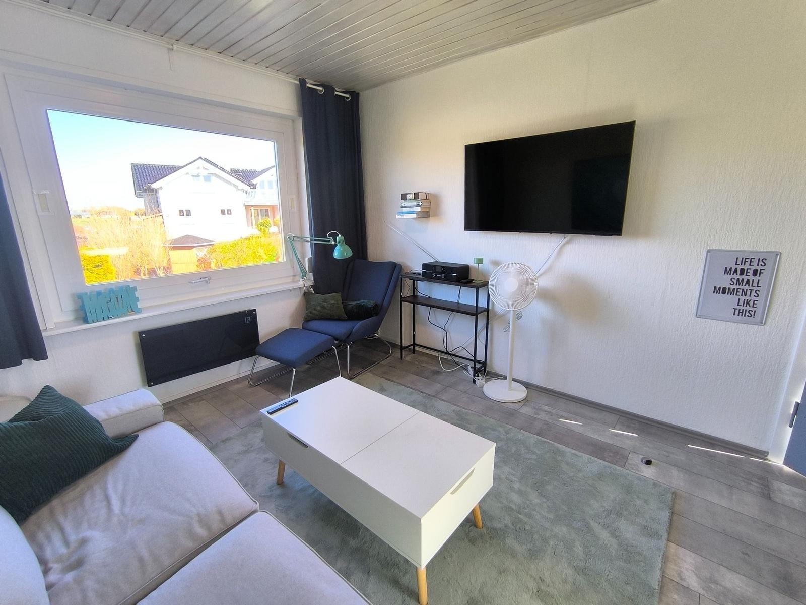 Wohnzimmer mit Sofa, Fernseher und Fensterblick auf Häuser.