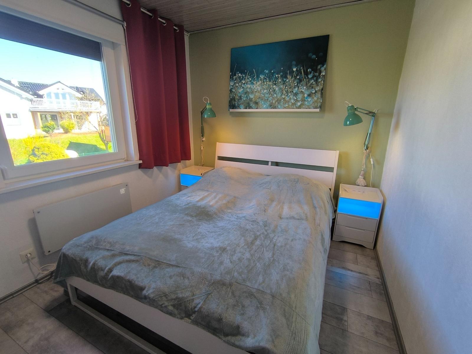 Schlafzimmer mit Bett, Nachttischen und Fensterblick auf Garten