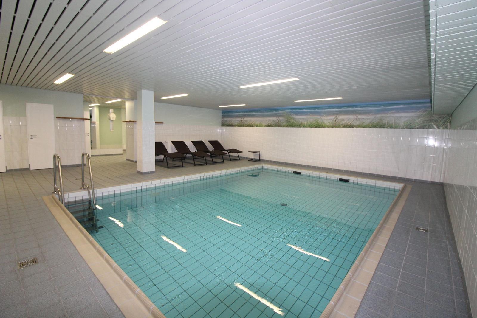 Indirektes Licht beleuchtet den Poolbereich mit Liegestühlen und Wandbild.