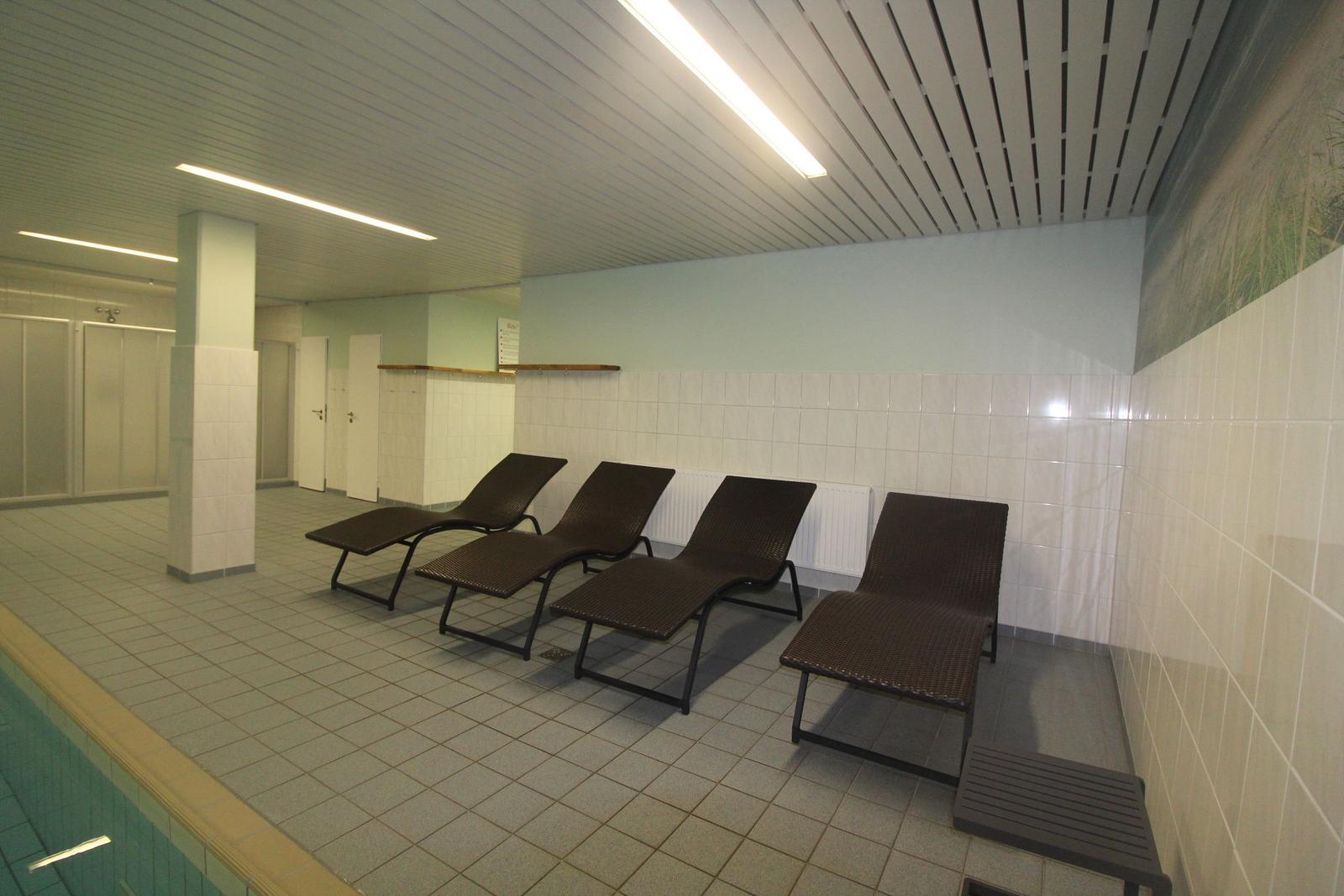 Raum mit Liegen neben Pool und Duschen im Hintergrund.