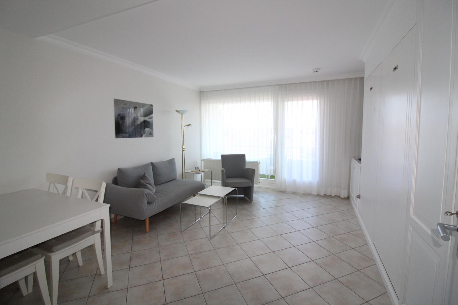 Wohn- und Essbereich mit Sofa, Stuhl, Tisch und Fenster mit Vorhängen.