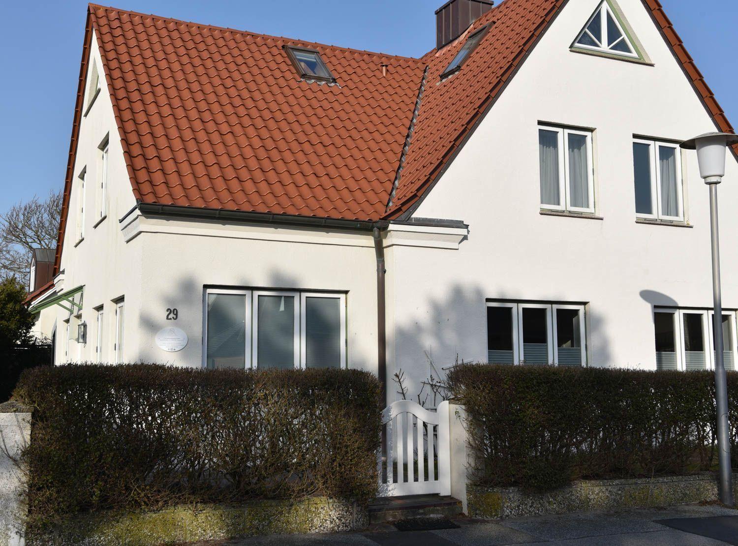 Weißes Haus mit rotem Ziegeldach und weißen Fenstern. Vorgarten mit Hecke und weißer Tür.
