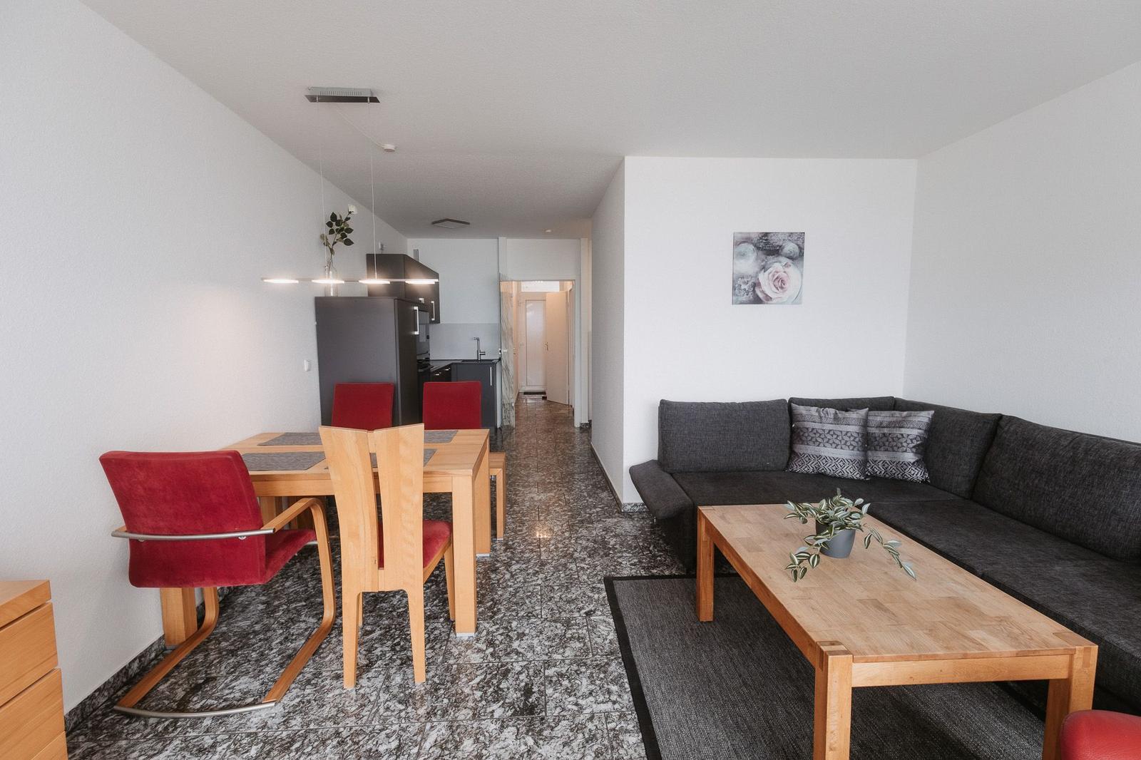 Wohn- und Essbereich mit Sofa, Tisch und Stühlen. Küche im Hintergrund.