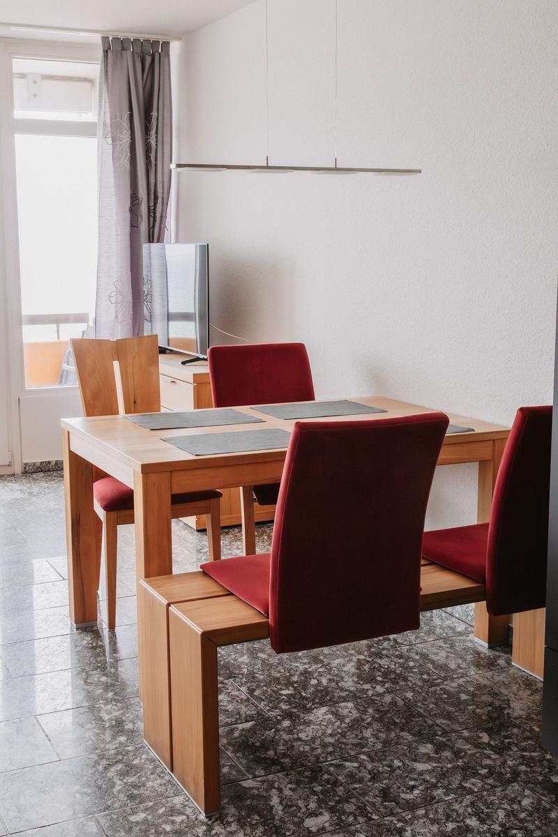 Esszimmer mit Holztisch, roten Stühlen und Fenster mit Vorhang.