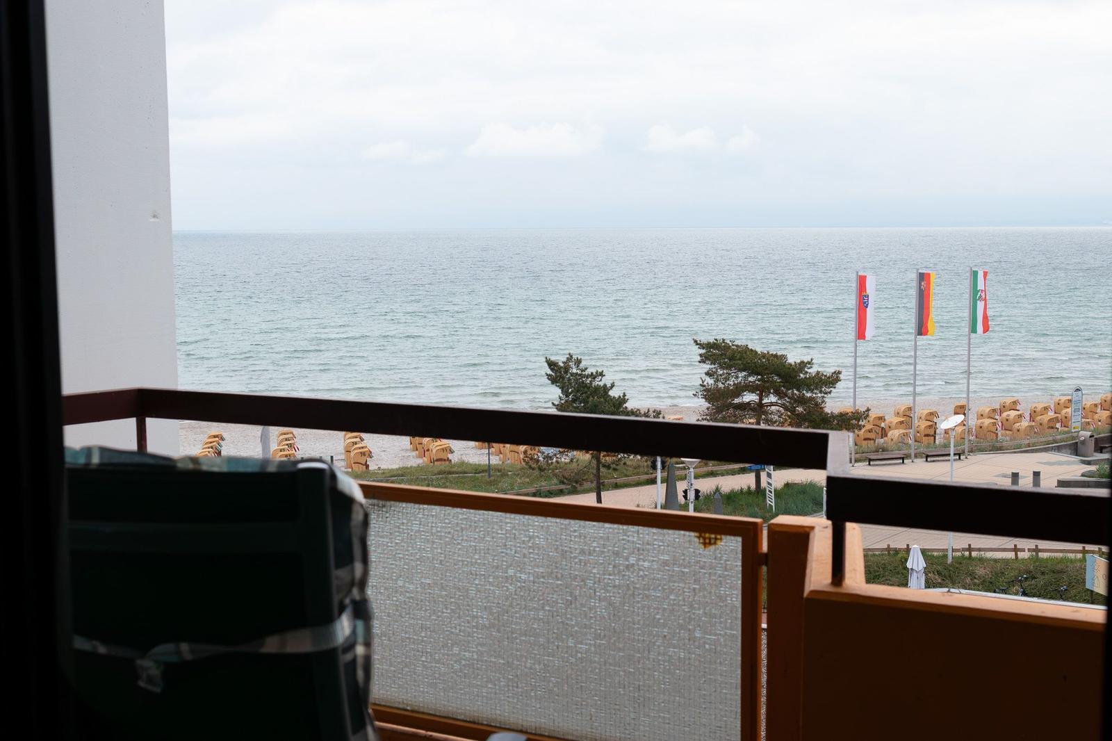 Blick von Balkon auf Strand mit Strandkörben und Flaggen