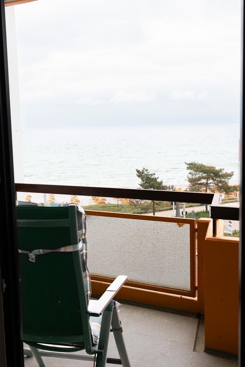 Balkon mit Stuhl und Meerblick. Geländer und Strand sind sichtbar.