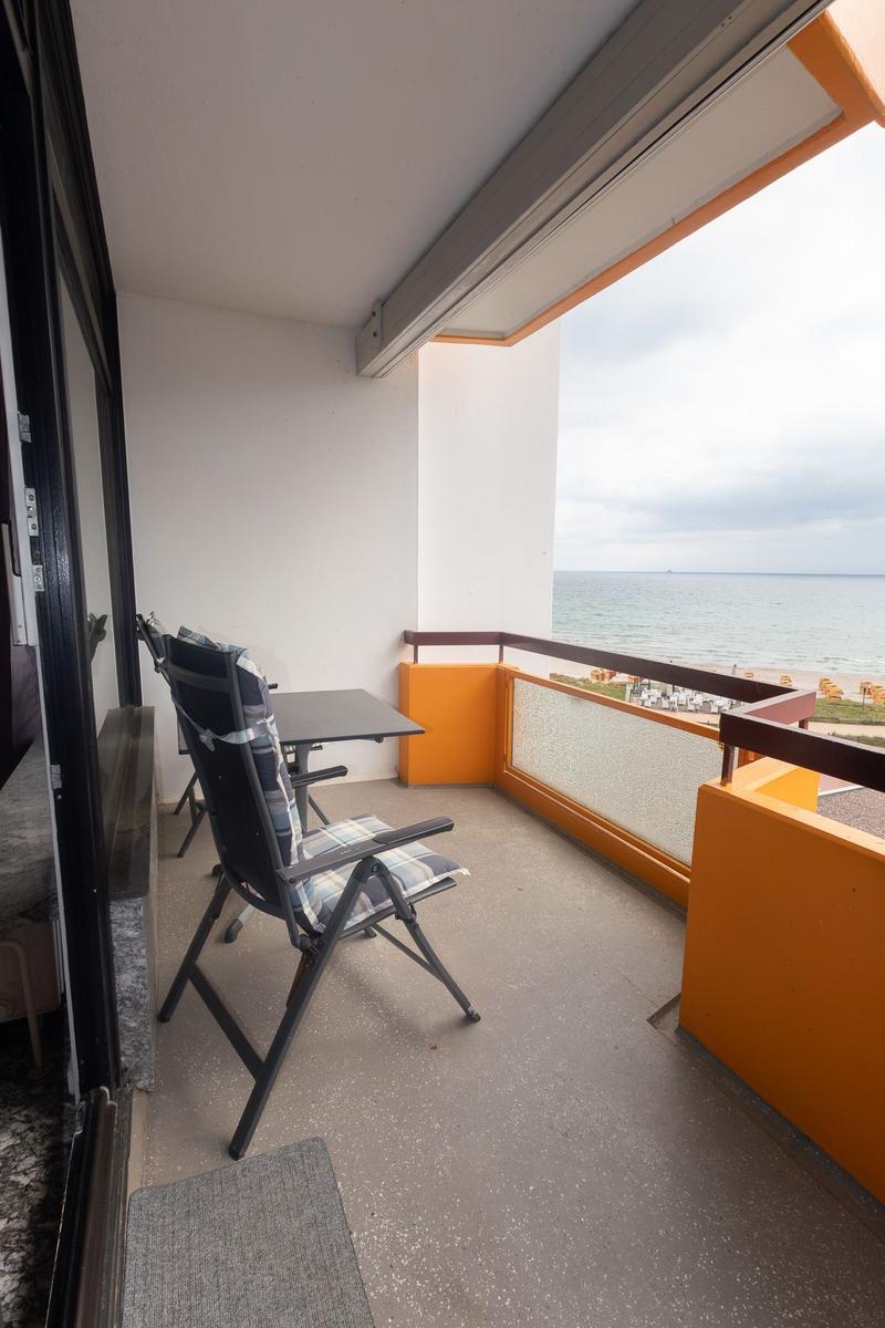Balkon mit Sitzgelegenheit und Meerblick. Geländer in Orange. Terrasse mit Tisch und Stühlen.