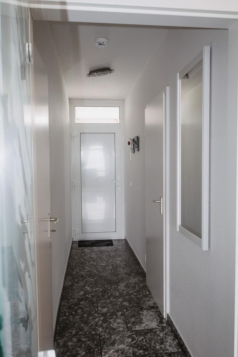 Flur mit dunklem Marmorfußboden, weißen Wänden und Türen. An der Wand hängt ein Spiegel.