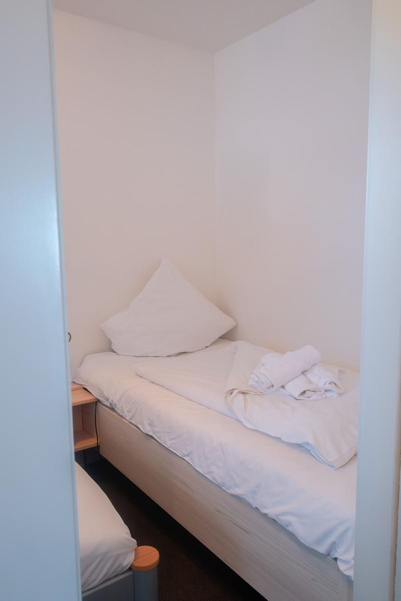 Ein Bett mit weißer Bettwäsche und einem Kissen in einem Raum mit weißen Wänden.