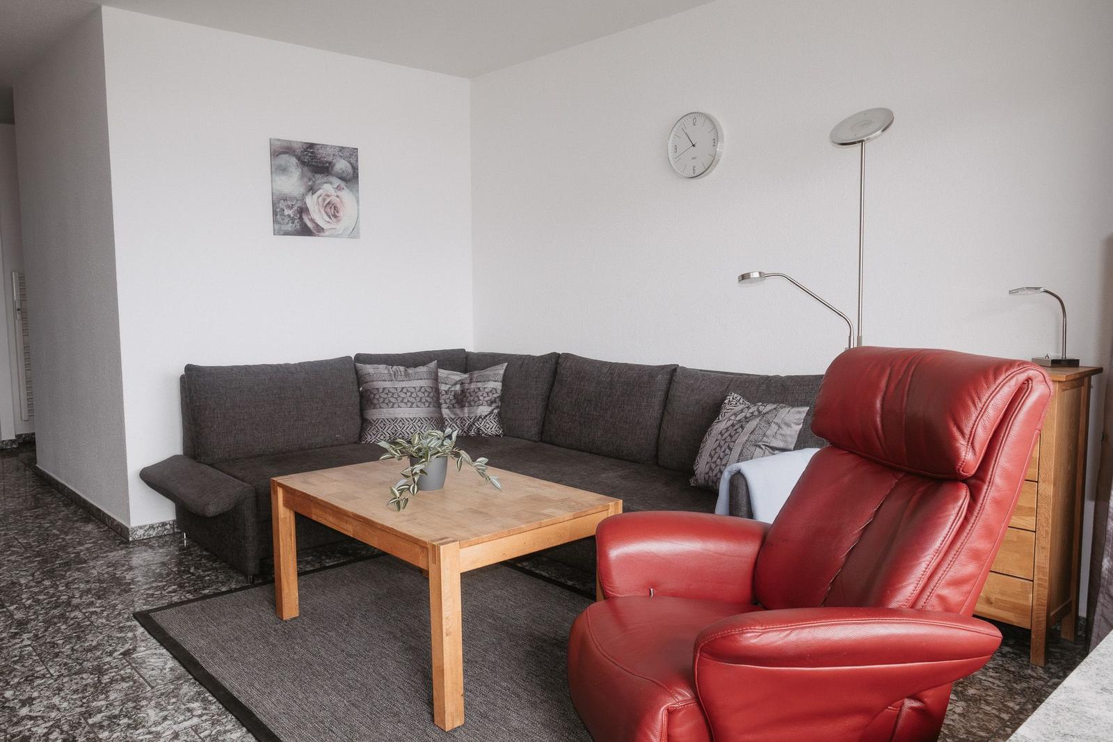Wohnzimmer mit grauem Sofa, rotem Sessel und Holztisch.