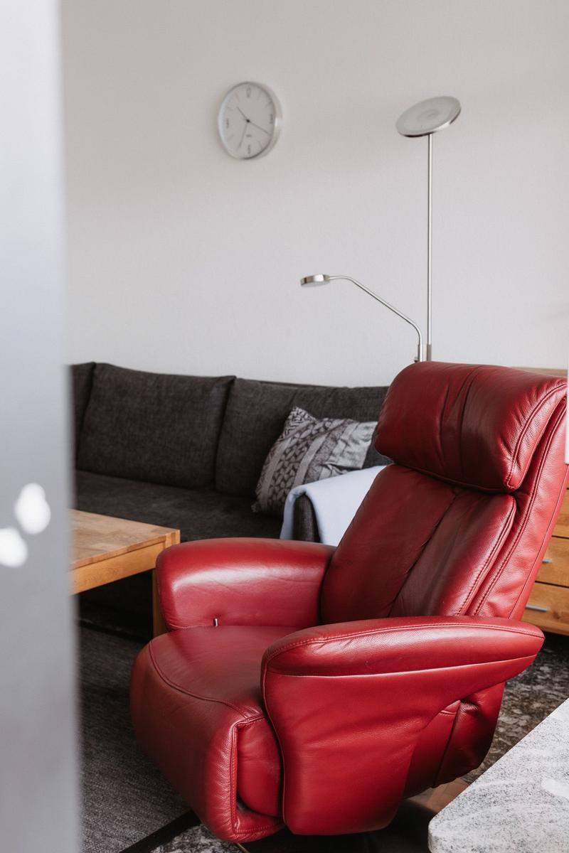 Ein roter Ledersessel steht im Wohnzimmer vor einem grauen Sofa.