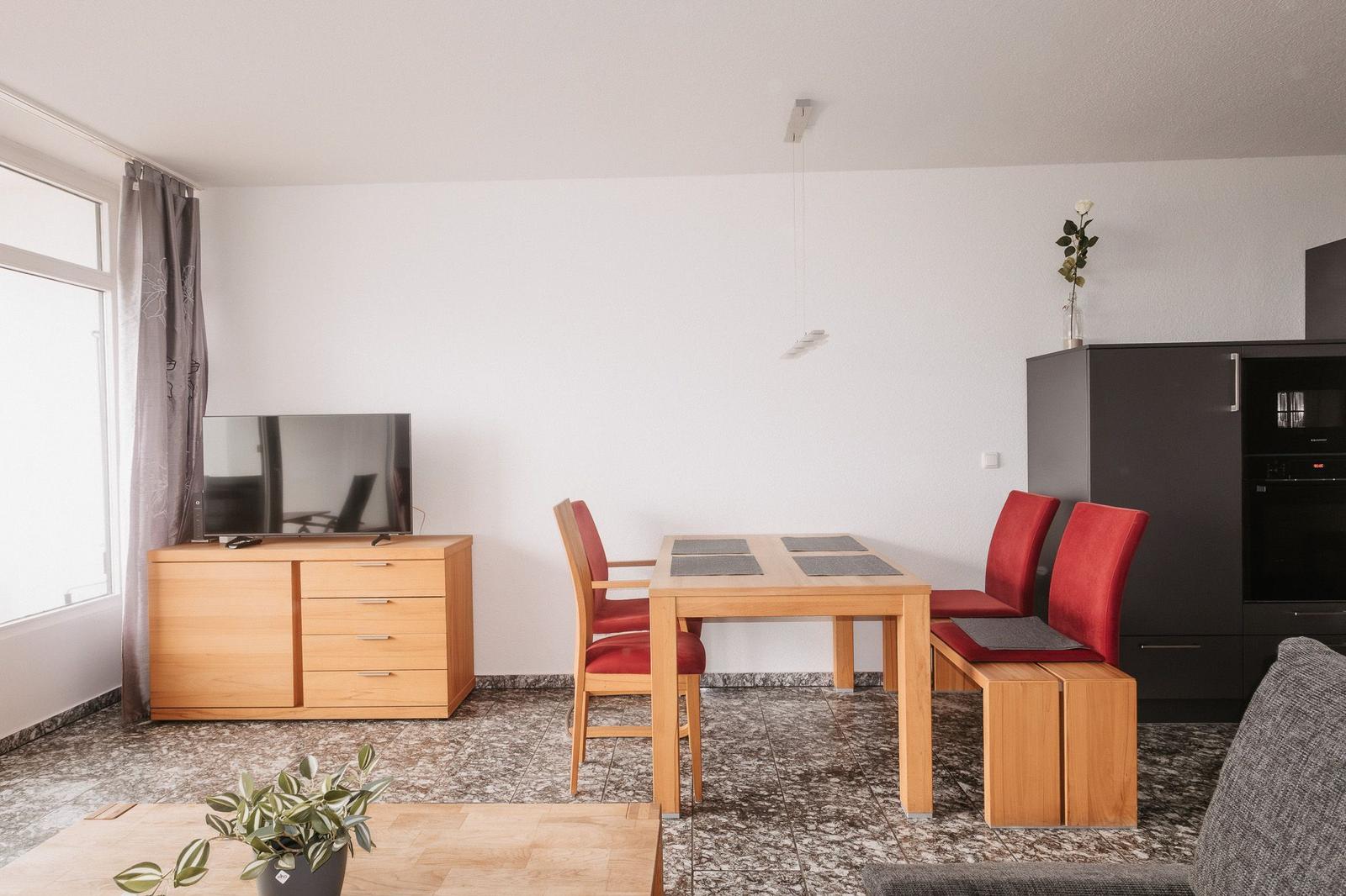 Essbereich mit Holztisch, roten Stühlen und dunklem Sideboard.