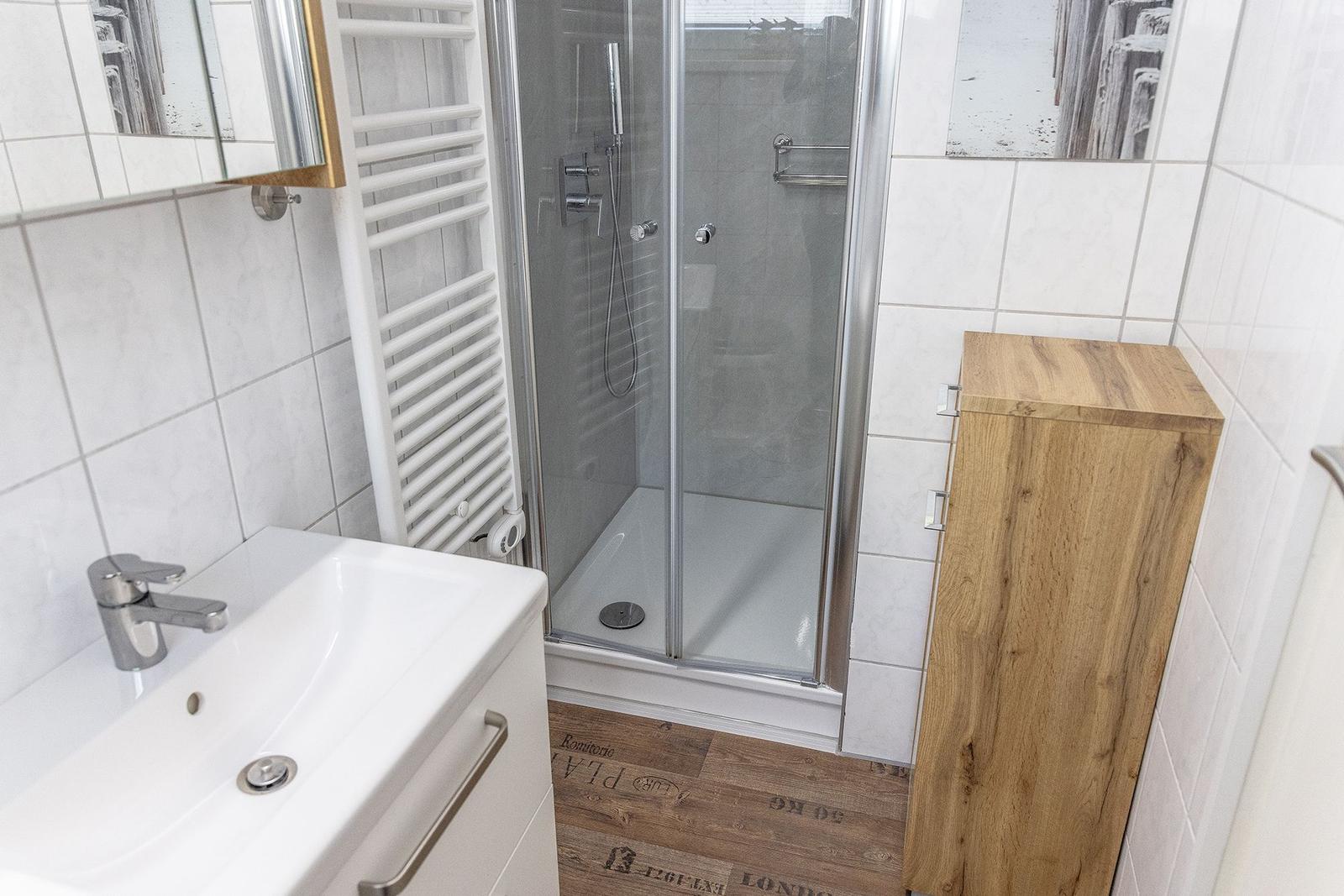Badezimmer mit Dusche, Waschbecken und Holzschrank.
