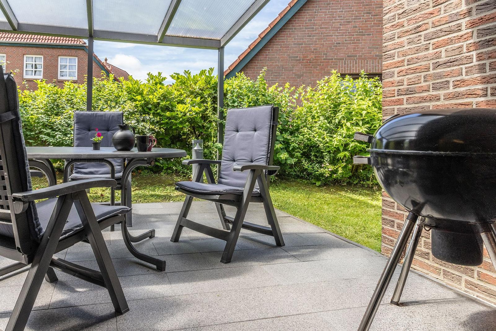 Terrasse mit Sitzgruppe, Grill und grüner Hecke. Überdacht mit Glasdach.