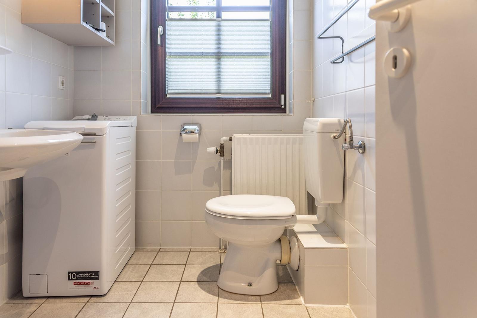 Badezimmer mit Toilette, Waschmaschine und Fenster