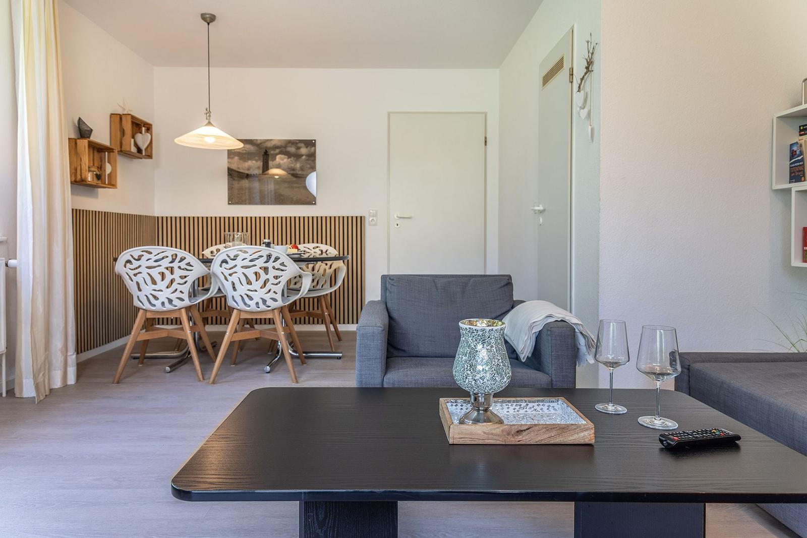 Wohn- und Essbereich mit Sofa, Tisch und Stühlen. Wandbild und Holzverkleidung sichtbar.