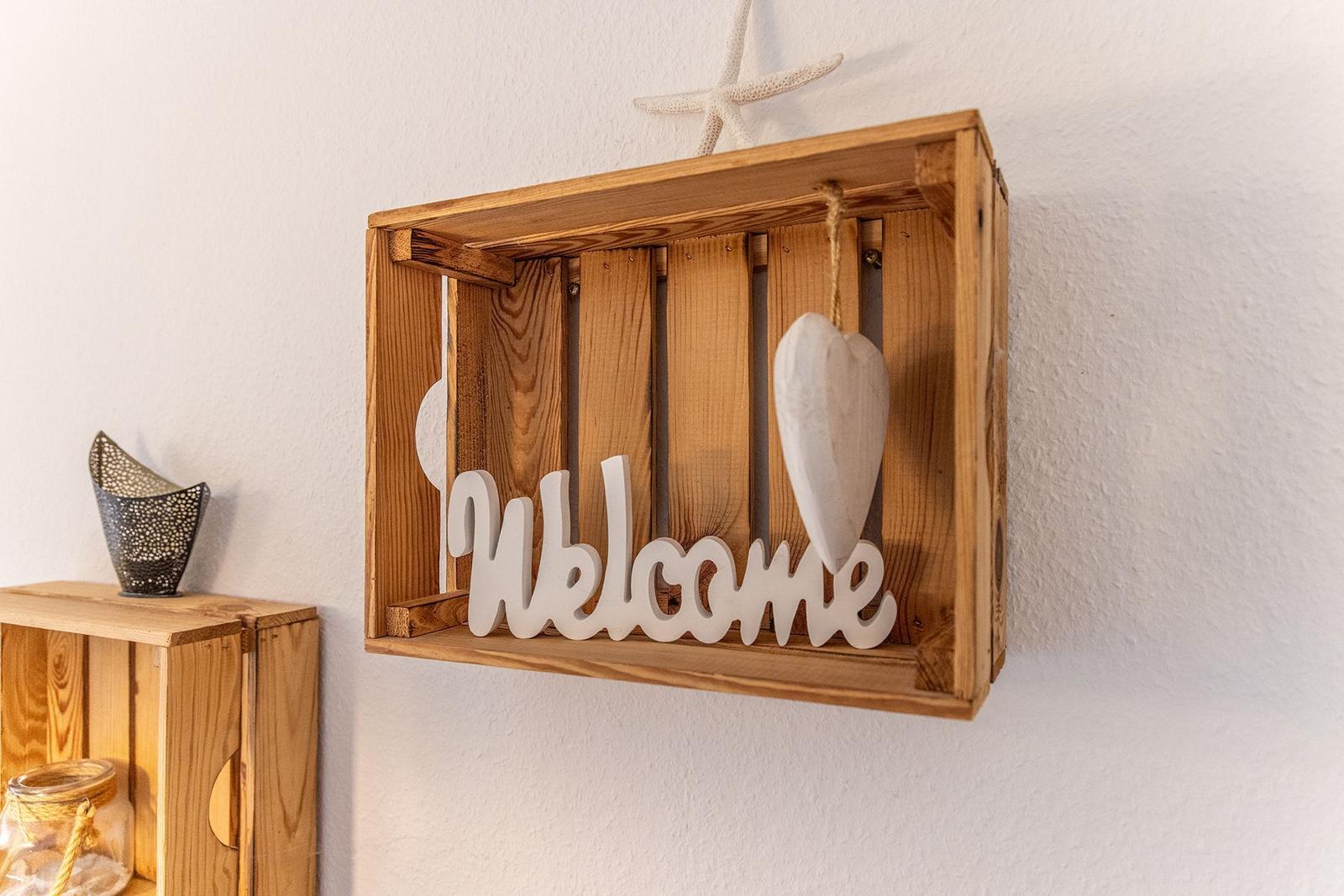 Holzkiste mit Welcome-Schild und Herz an der Wand