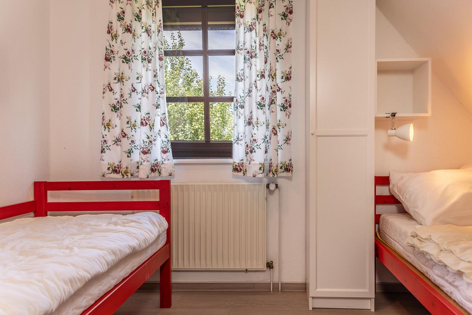 Zwei Schlafzimmer mit roten Betten und floralen Vorhängen an einem Fenster.