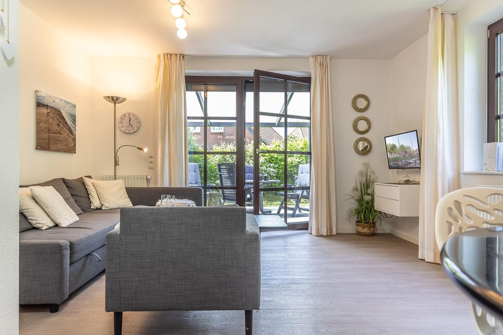 Wohnzimmer mit Sofa, Sessel und Blick auf Terrasse.
