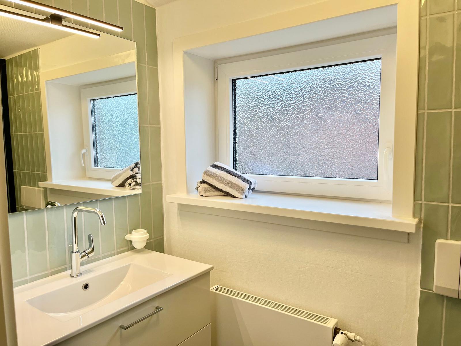 Badezimmer mit Waschbecken, Spiegel und Fenster mit gefrosterter Scheibe.