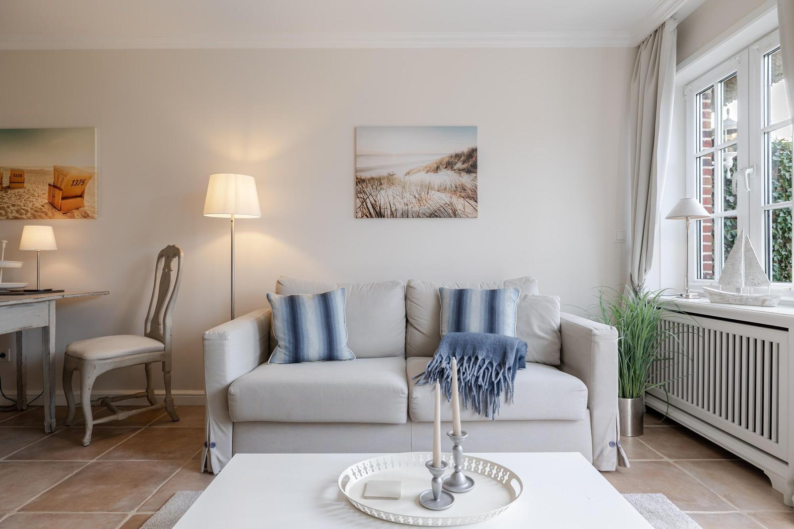 Wohnzimmer mit Sofa, Tisch, Wandbildern und Fenster mit Blick.