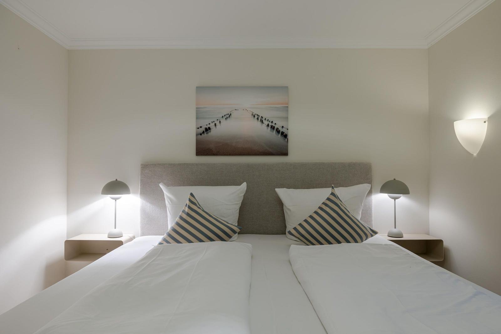 Schlafzimmer mit Doppelbett, zwei Nachttischen und Wandbild. Deckenleuchte und Wandlampen.