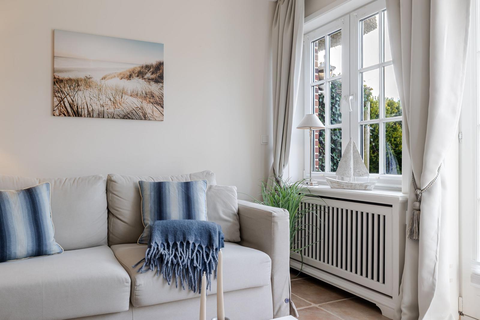 Ein Sofa mit Kissen und Decke vor einem Fenster mit Blick auf Grün.