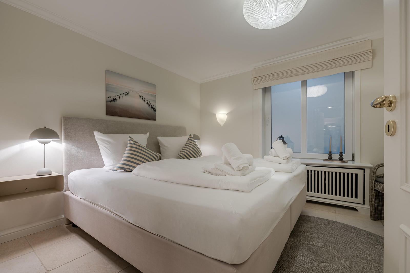 Schlafzimmer mit Bett, Nachttisch, Wandbild und Fenster mit Blick.