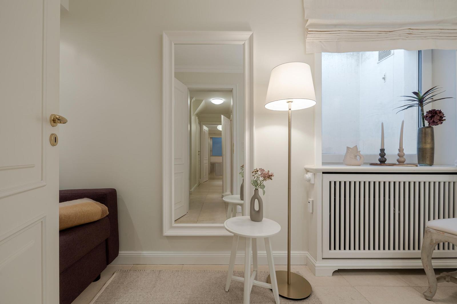 Eingangsbereich mit Spiegel, Stehlampe und Fenster mit Pflanzen.
