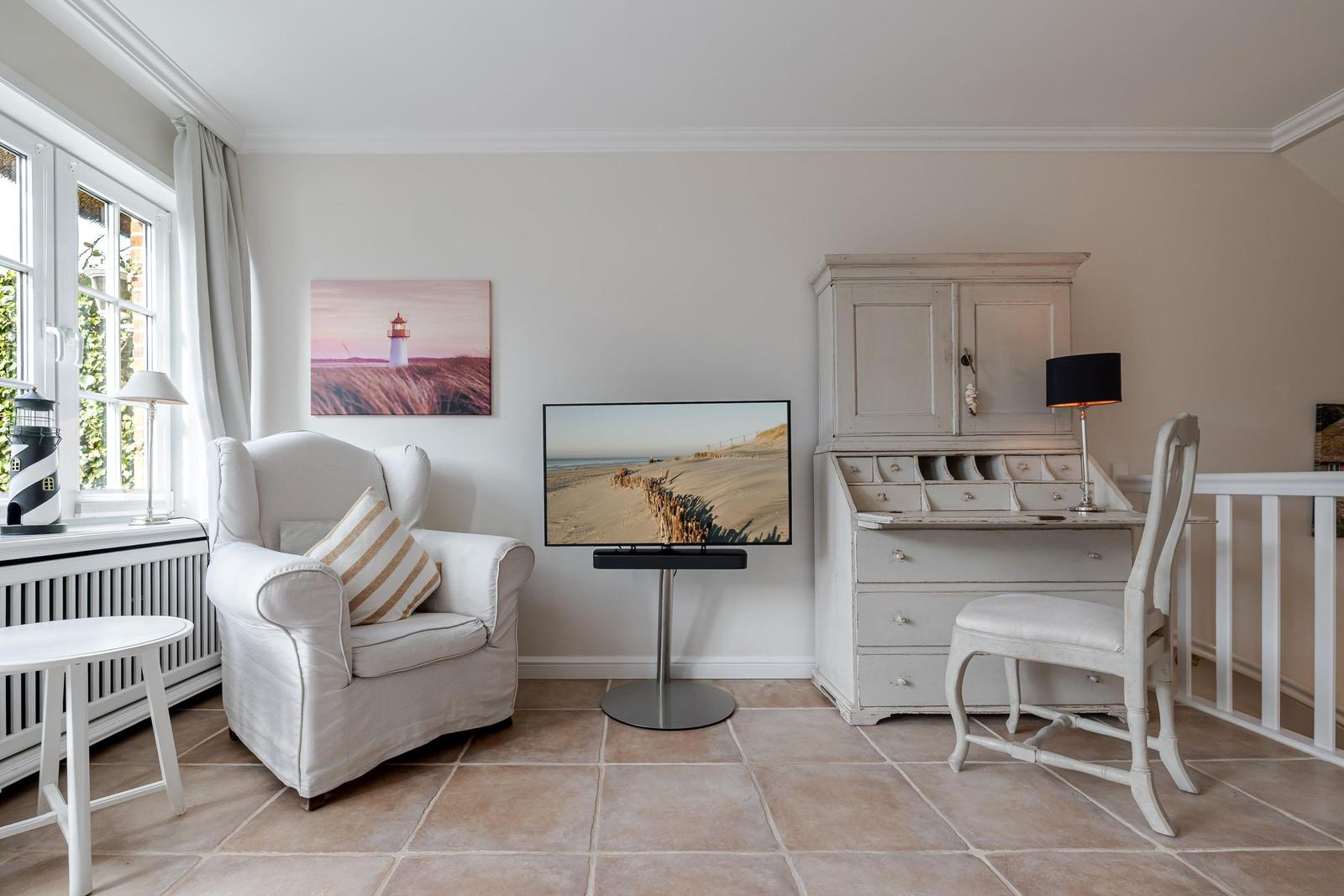 Ein Raum mit Sessel, Fernseher und Schreibtisch mit Stuhl.
