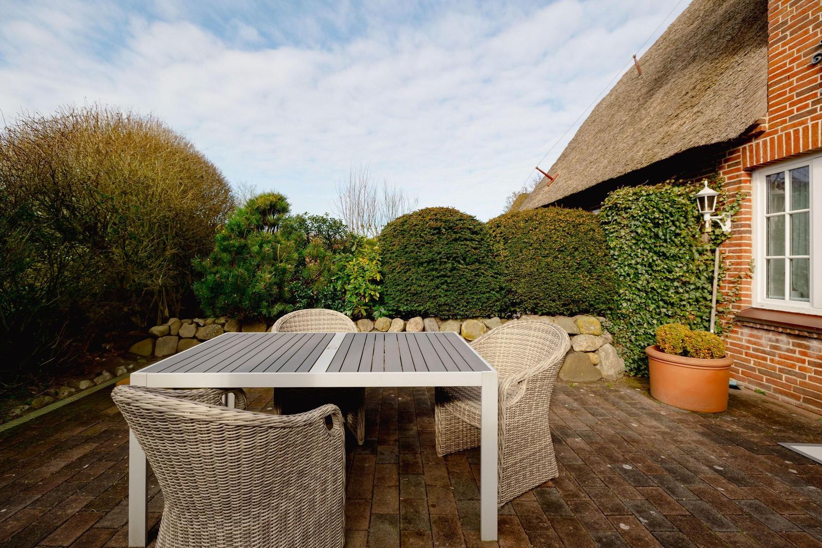 Terrasse mit Tisch und Stühlen neben einem Haus mit strohgedecktem Dach.