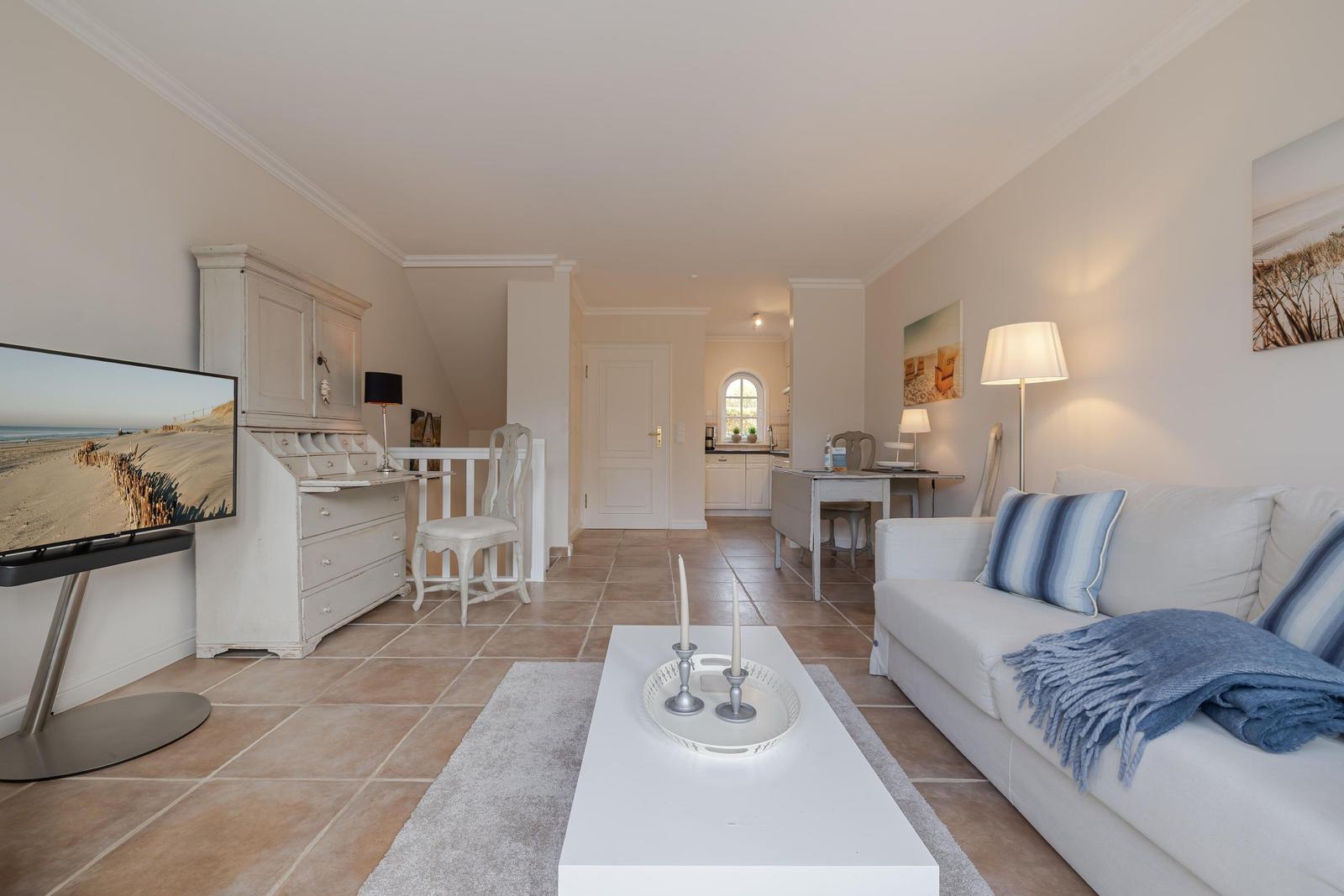 Wohnzimmer mit Sofa, Couchtisch und Fernseher. Küche und Schlafzimmer im Hintergrund.