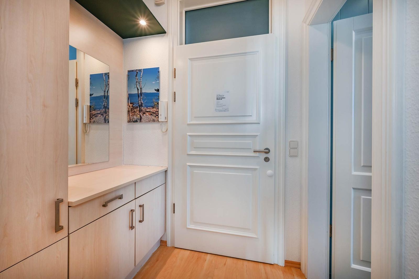 Hausgang mit weißen Türen, Holzboden und Schrank mit Spiegel.