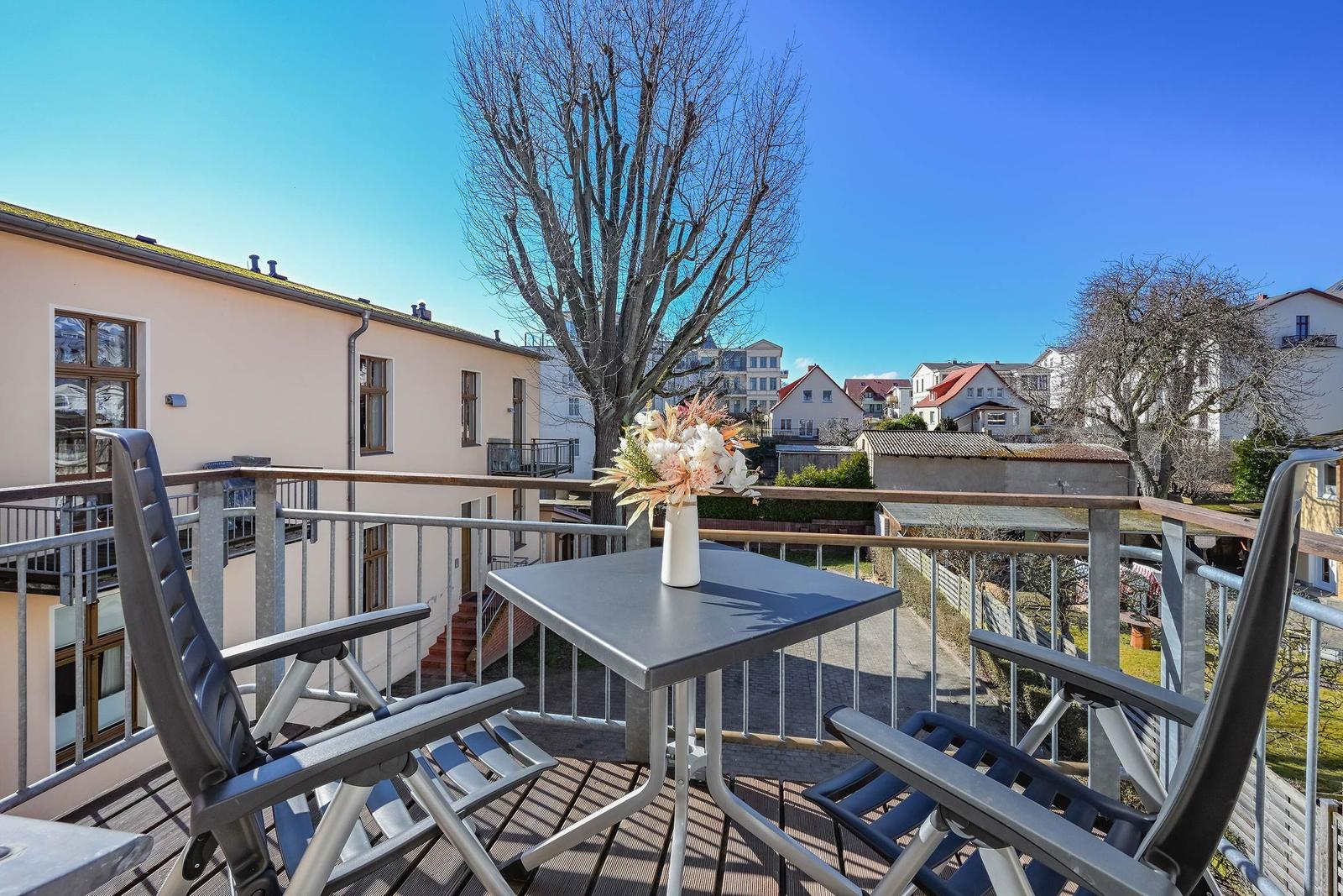 Terrasse mit Tisch und zwei Stühlen, Blick auf Wohnhäuser und einen Baum.