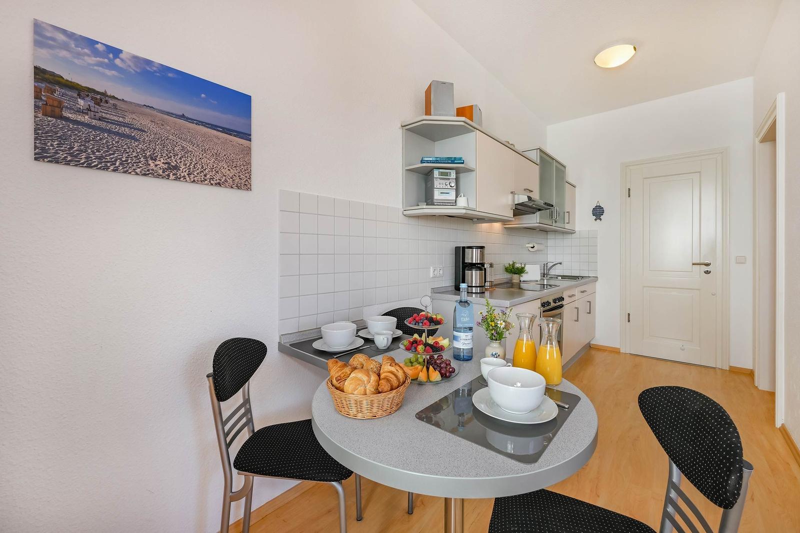 Küche mit Esstisch, Frühstückszubehör und Strandbild an der Wand.